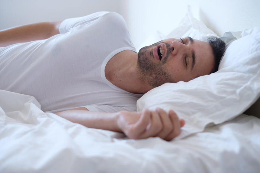 Man with obstructive sleeps apnea sleeps fitfully in white sheets