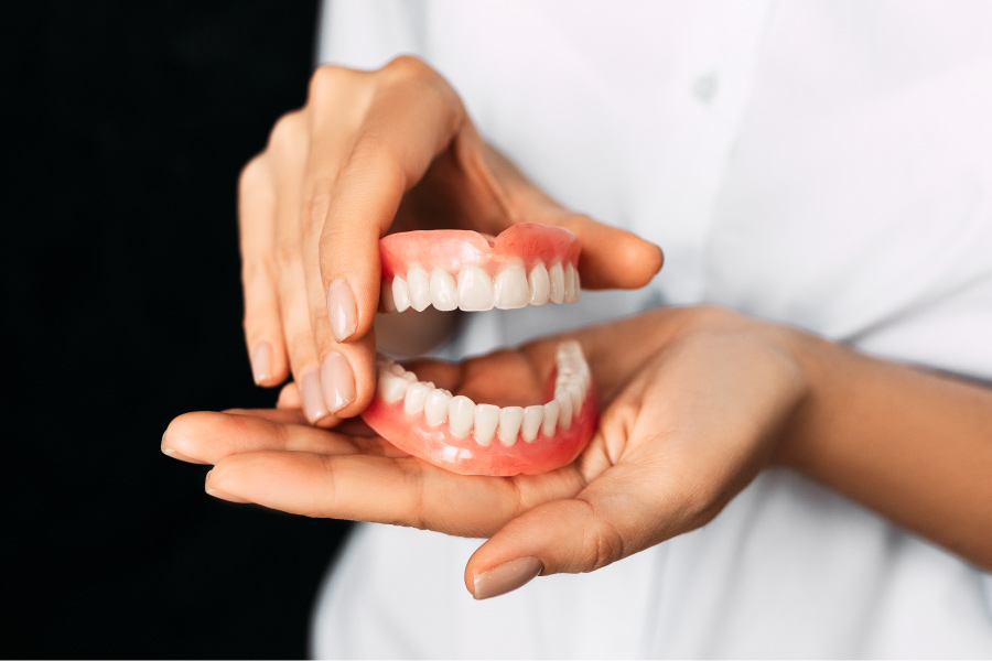 A prosthodontist holds a pair of dentures to show a patient their artificial teeth replacement