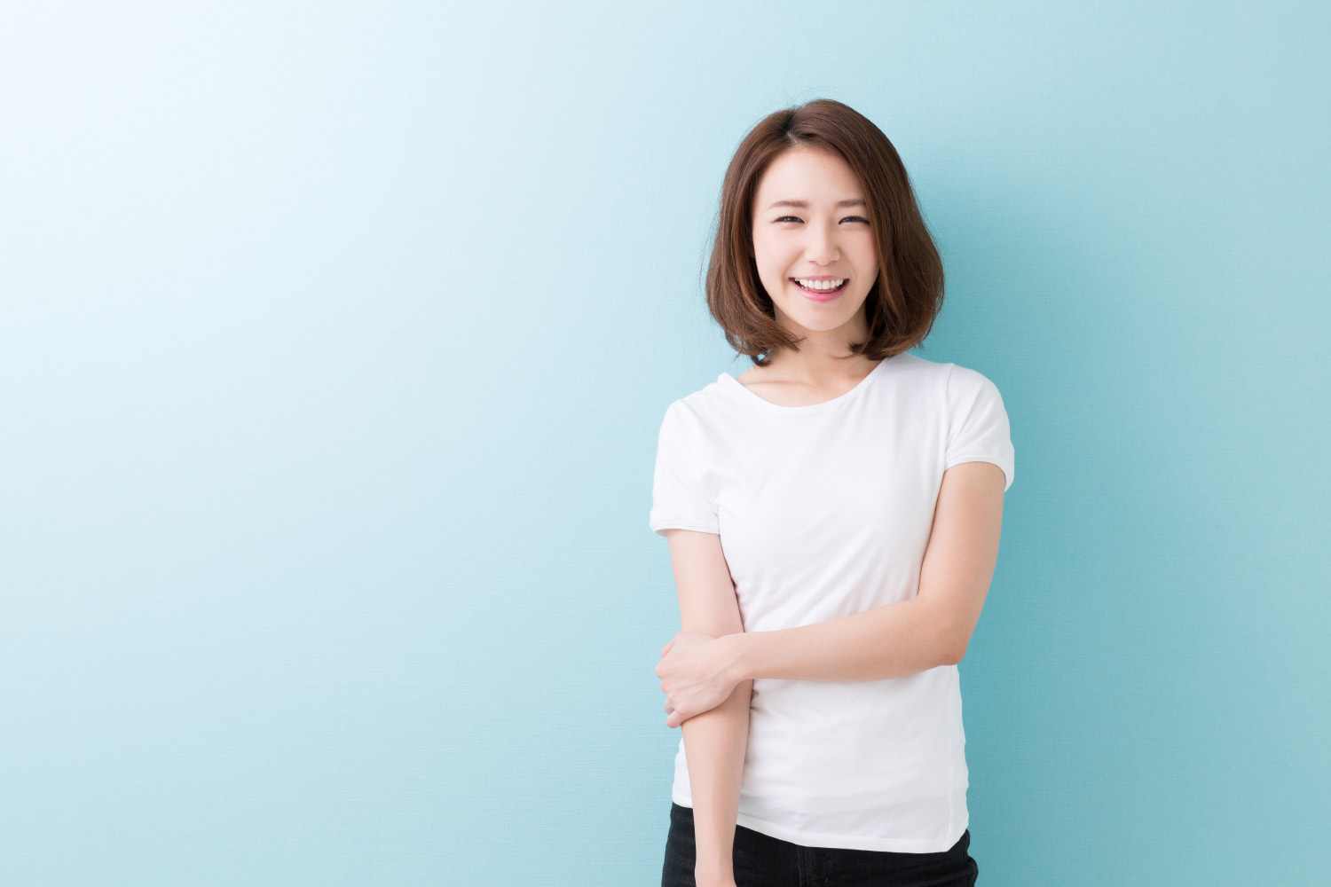 Brunette woman with veneers smiles against a blue wall while wearing a white t-shirt in Harrisonburg, VA