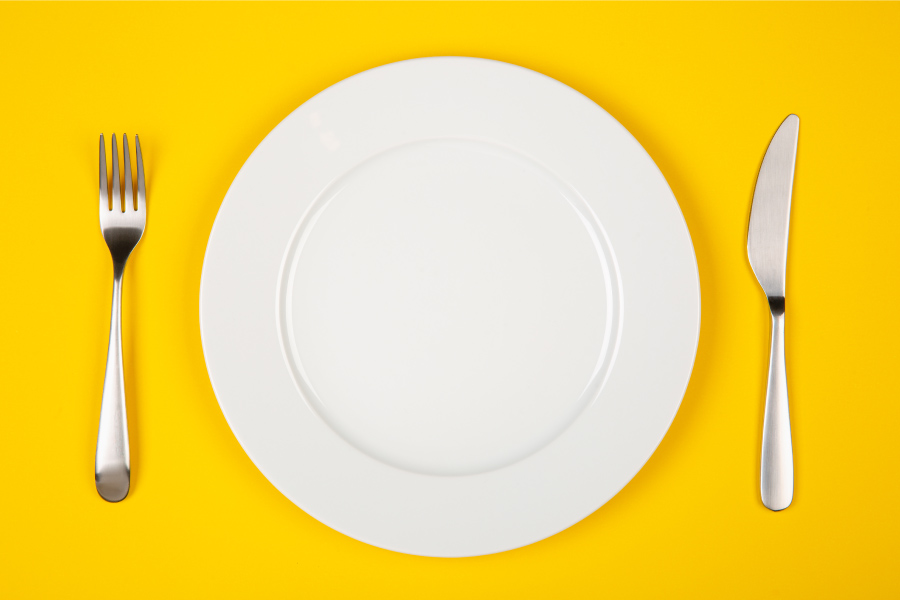 Aerial view of a white plate on a yellow table about to be filled with fall foods