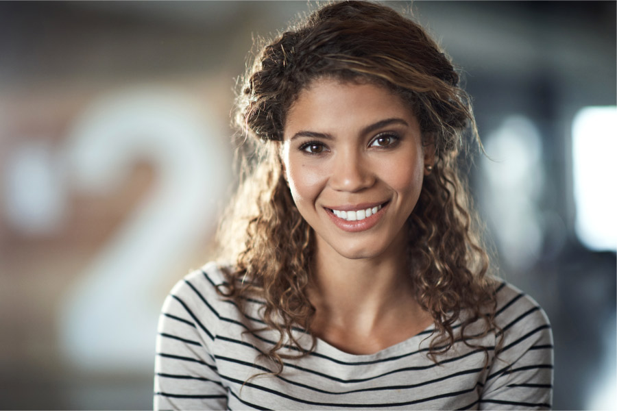 Curly brunette woman smiles after visiting her prosthodontist in Harrisonburg, VA.