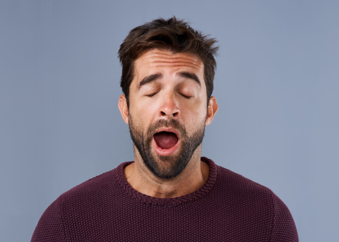 Brunette man in a maroon shirt yawns because he has obstructive sleep apnea