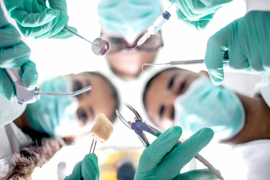 Looking up into several oral surgeons in teal scrubs and masks holding special tools