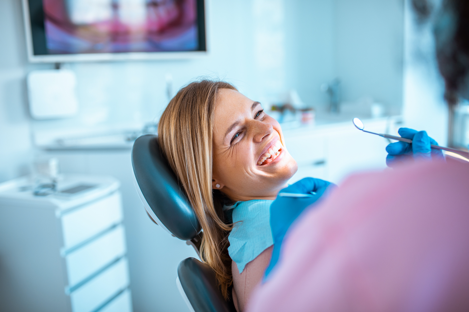 Blonde woman smiles while sitting in a dental chair at the dentist for her routine checkup and cleaning
